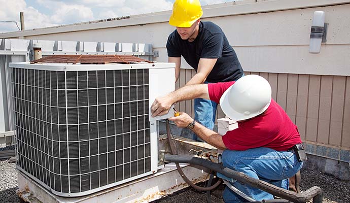 two individuals performing repair service on an outdoor air conditioning unit