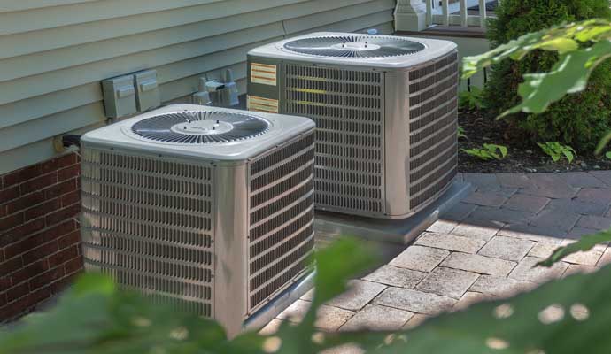 two central air conditioning  units placed on a paved area