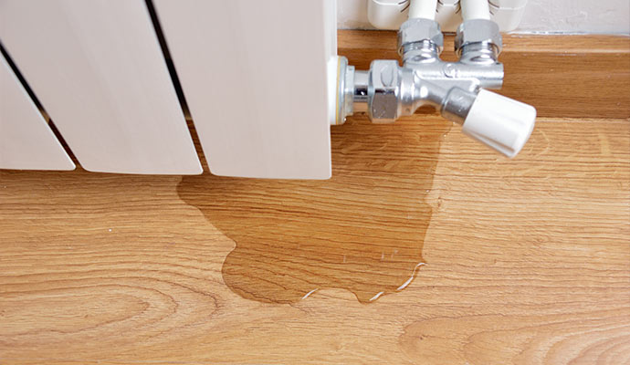 A leaking radiator is spraying water onto a wooden floor.